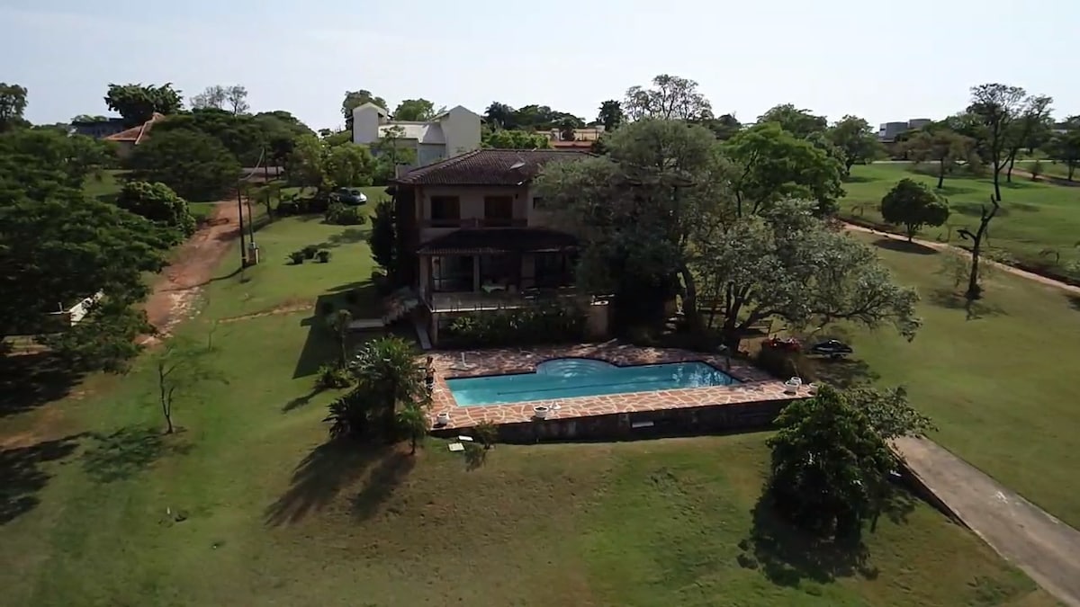 An aerial view captures a spacious property featuring a well-maintained garden, a private pool surrounded by stonework, and a two-story house set amidst trees. The pool area is complemented by ample outdoor space, creating an inviting environment for relaxation.