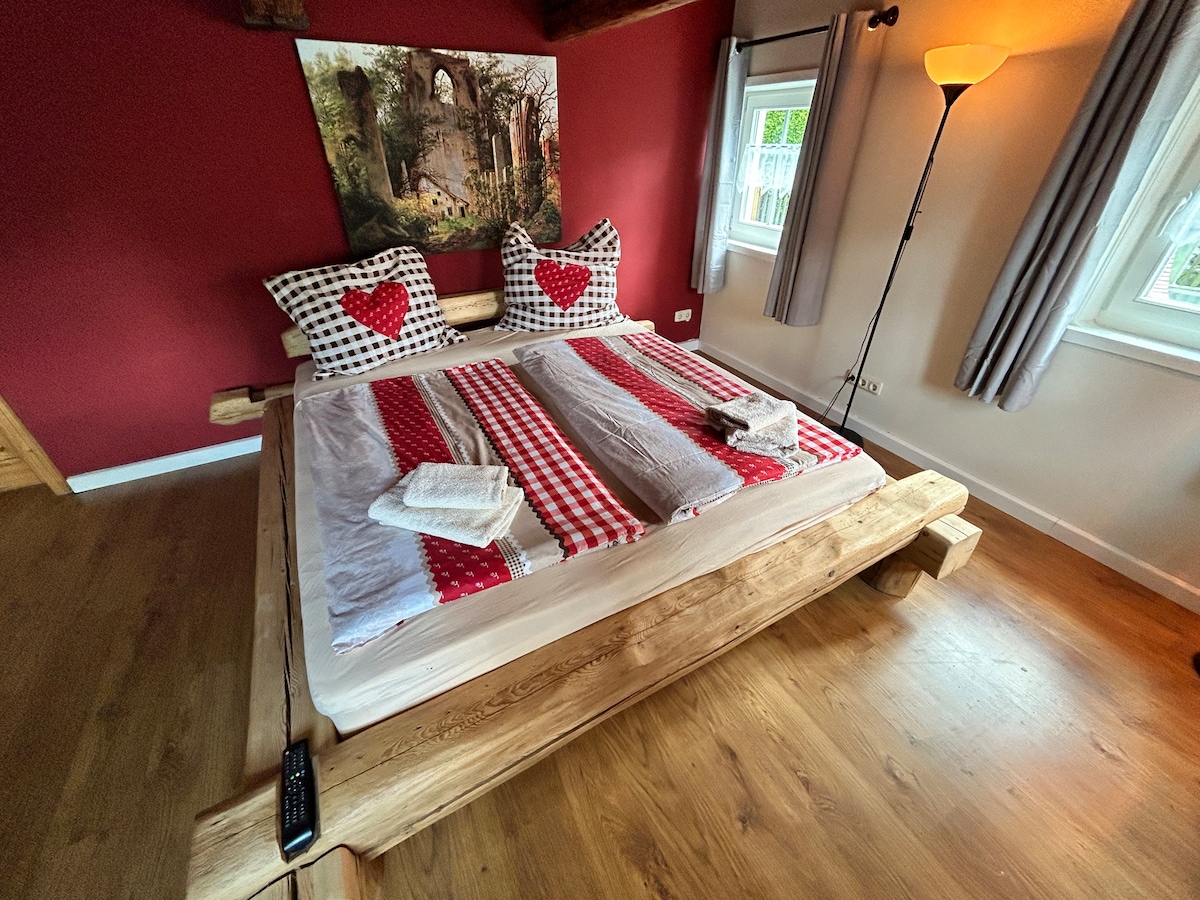 ห้องนอนขนาดใหญ่ (สำหรับครอบครัว) พร้อมเตียงไม้เก่าทำมือแบบชนบทสำหรับไม่เกิน 4 คน นี่คือเตียงคู่ขนาดใหญ่ (180x200 ซม.) และเตียงคู่ 1 หลัง (140x200 ซม.) มองเห็นแม่น้ำ Mandau