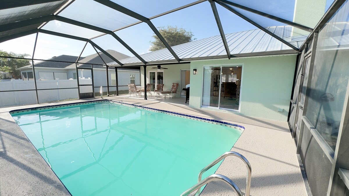 An inviting private pool area is enclosed by a screened lanai, providing a bright and airy atmosphere. The pool is surrounded by several lounge chairs, with easy access to the adjacent living space through sliding glass doors.