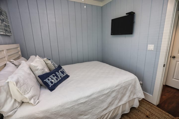 - მშვიდი საძინებელი რბილი თეთრი თეთრეულით, მყუდრო ბალიშებით და პლაჟისპირა აქცენტით
- კედელზე მიმაგრებული ტელევიზორი ხელს უწყობს საწოლში ფილმის გადაღებას
- სუფთა ხაზები და დამამშვიდებელი ფერები აქცევს მშვიდ დასვენებას მზის სხივებით სავსე დღეების შემდეგ