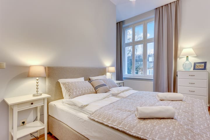 Dhomë gjumi me krevat dopio, tavolinë pranë krevatit dhe abazhur.