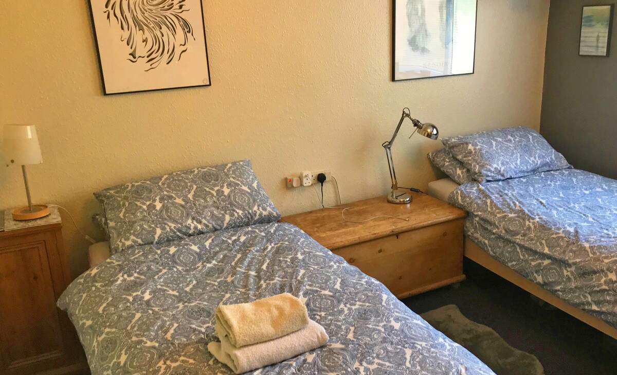 Spavaća soba s dva kreveta za jednu osobu, noćnim ormarićima i svjetlima za čitanje. 