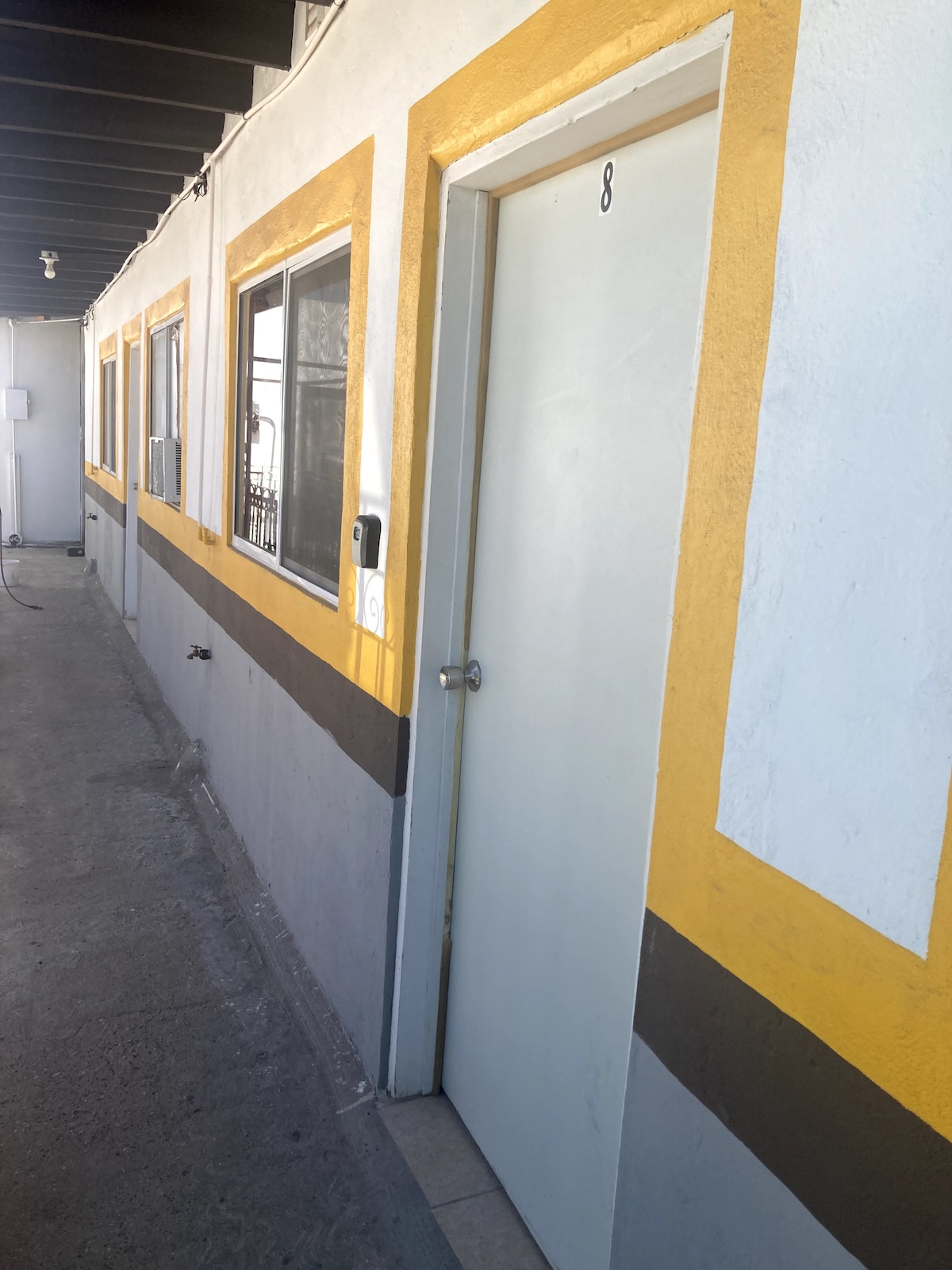 The image displays a corridor of a building with a vibrant color scheme, featuring several doors. The door numbered 8 is highlighted, flanked by windows. The corridor is well-lit, showcasing a clean and accessible pathway.