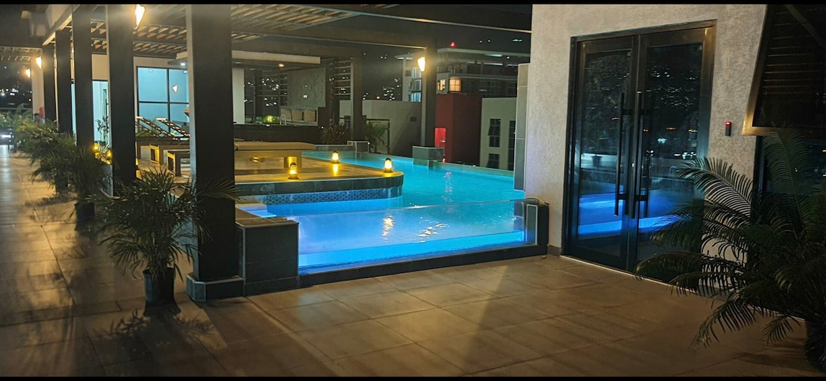 An inviting swimming pool is surrounded by modern lounge seating and potted plants. Soft lighting enhances the water's glow, reflecting off the tiles. The sliding glass doors lead to a spacious indoor area, providing a seamless transition between spaces.
