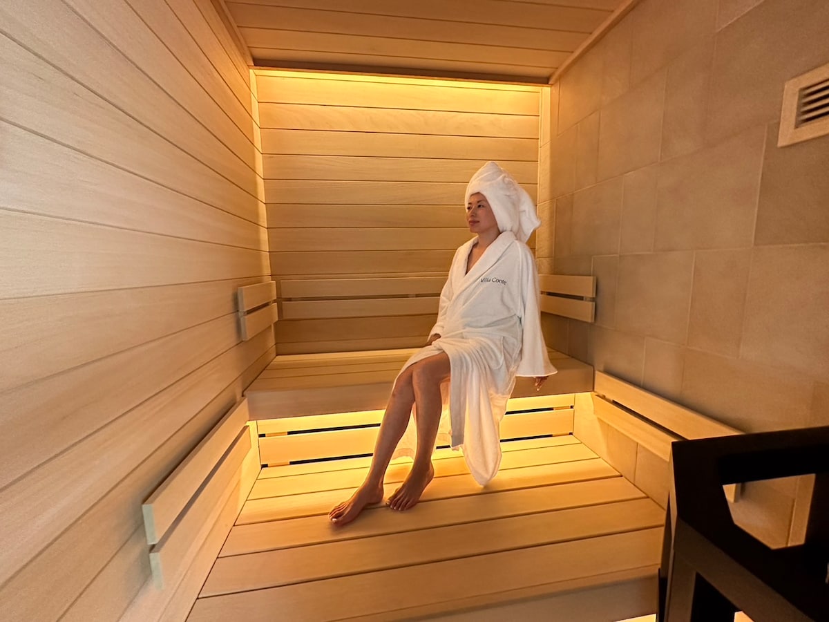 A spacious sauna interior is displayed, featuring wooden benches aligned on two tiers. Soft ambient lighting creates a calming environment. The warm wood tones highlight the sauna's clean lines and modern design, inviting relaxation and rejuvenation.