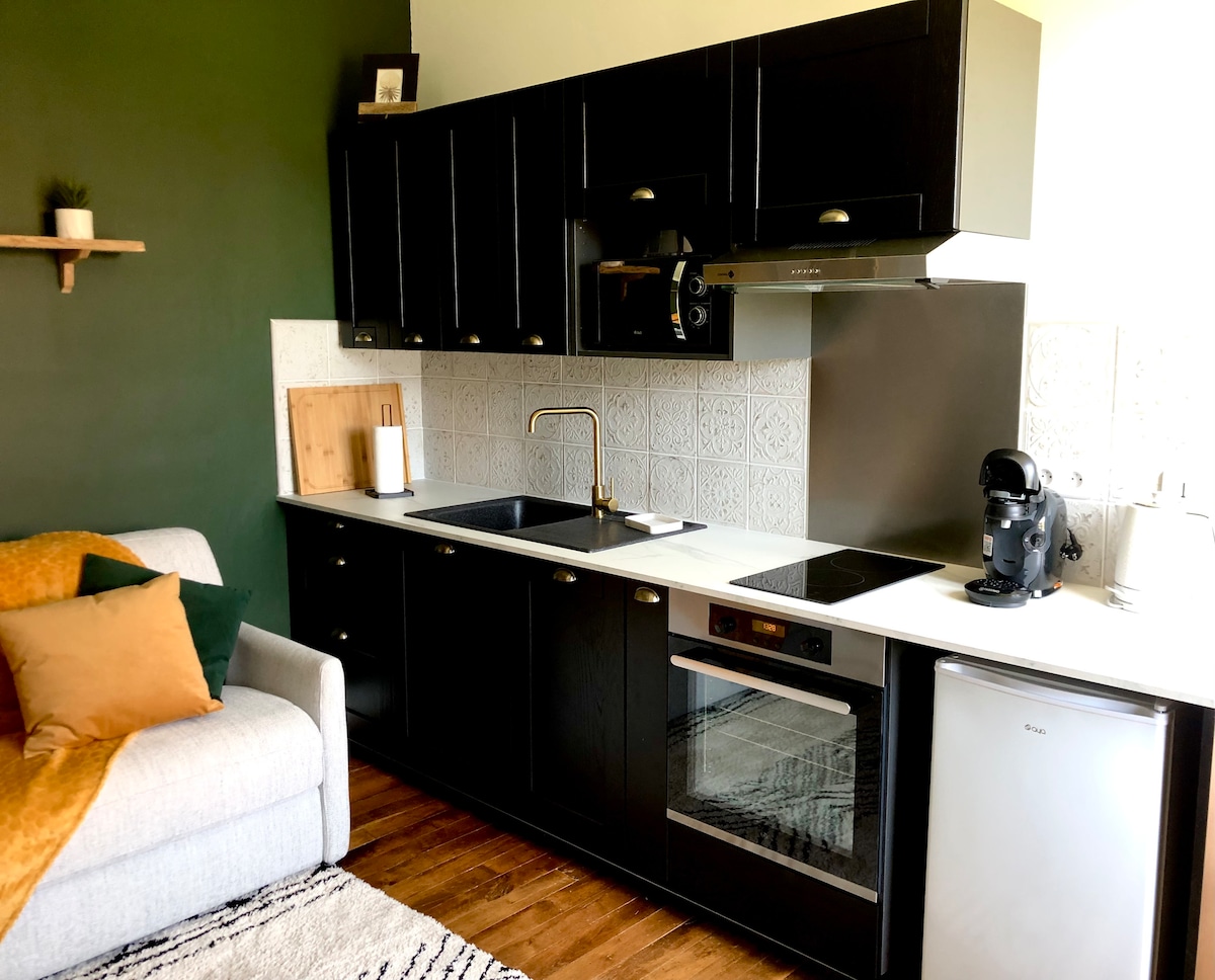 A modern kitchen area features dark cabinetry and light countertops, providing ample storage and prep space. A convenient cooktop, oven, and a compact refrigerator are included. A sofa with colorful cushions is positioned nearby, adding to the cozy atmosphere of the space.