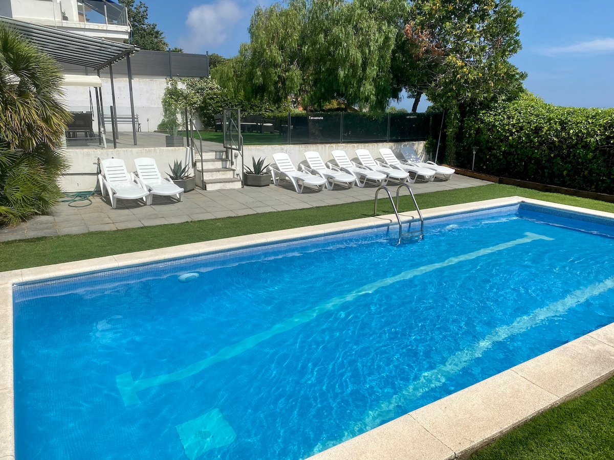 A large swimming pool is surrounded by a spacious patio area, featuring several lounge chairs arranged neatly along one side. Lush greenery and well-maintained shrubs provide privacy and enhance the serene outdoor setting.