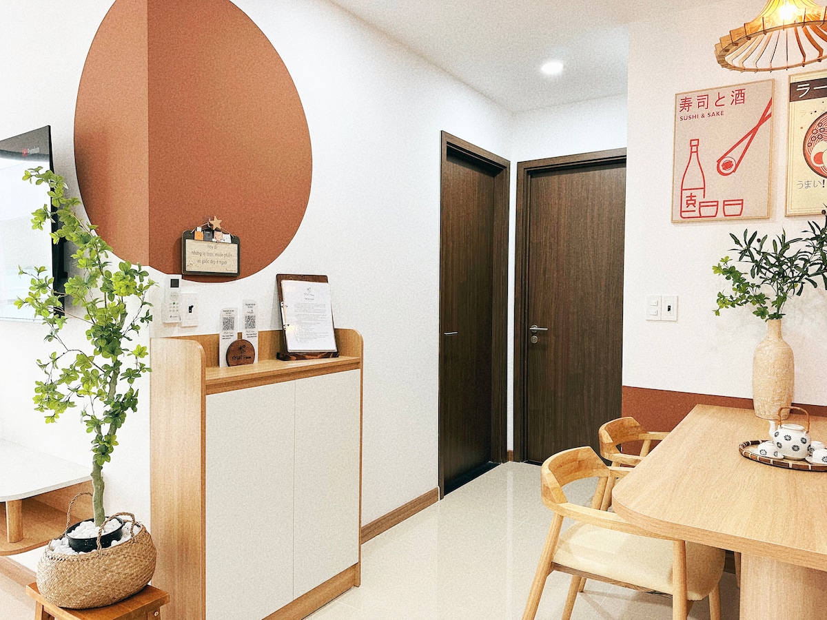 A modern entryway is showcased, featuring a sleek console table with decorative items. A dining area with wooden chairs is visible, along with a charming wall featuring artwork and a round accent painted in earthy tones. Two doors lead to separate rooms.