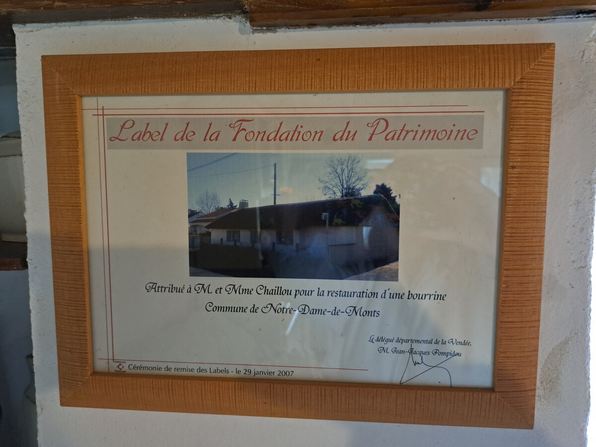A framed certificate from the Foundation of Heritage is displayed, recognizing Mr. and Mrs. Chaillon for their restoration work on a bourrine in Notre-Dame-de-Monts. The certificate features an image of the structure, surrounded by a wooden frame and decorative border.