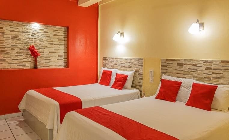 A comfortable sleeping area is presented with two spacious beds, each adorned with white linens and red accent pillows. A textured stone wall feature adds visual interest, while soft lighting from wall sconces enhances the warm ambiance.