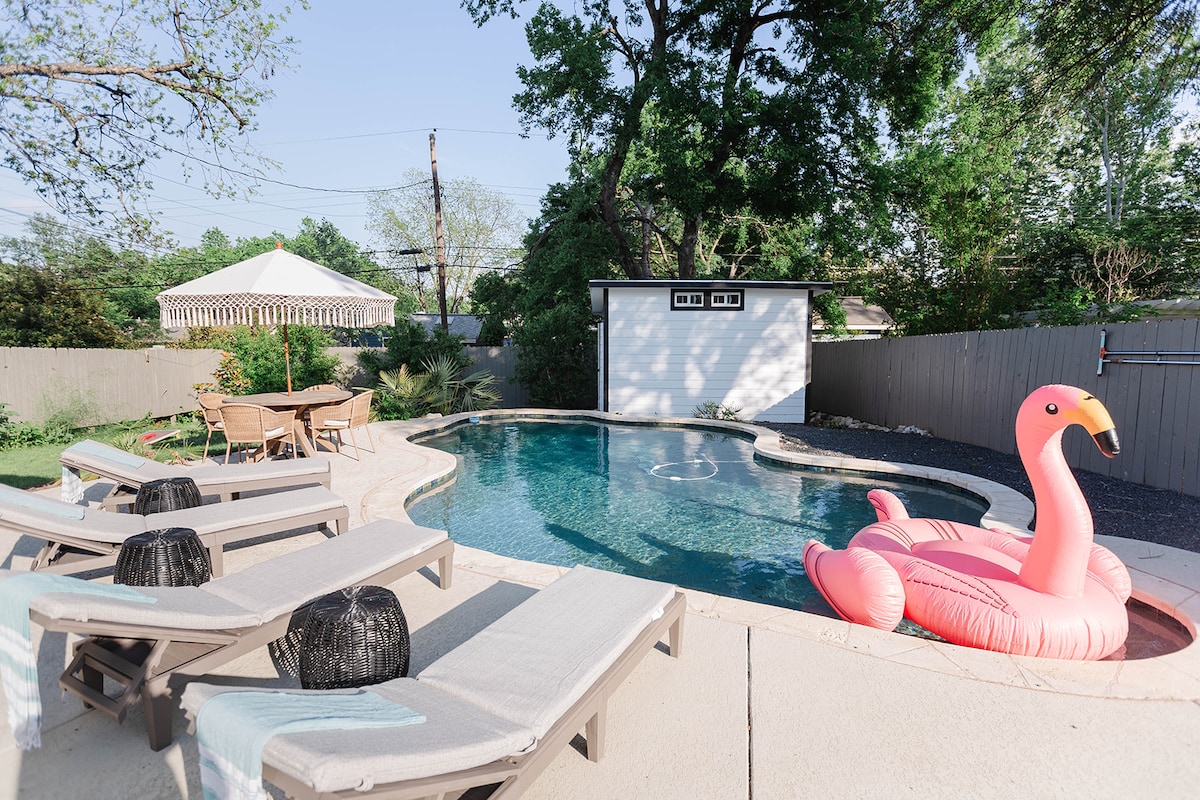 A private outdoor space features a serene pool surrounded by loungers. A pink flamingo float adds a playful touch. Nearby, a shaded seating area under a gazebo provides a relaxing spot, while the lush greenery offers a backdrop of natural beauty and privacy.