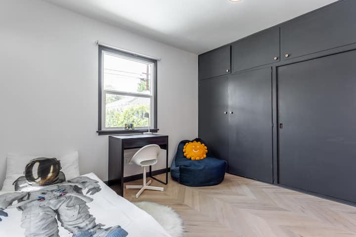 Quarto para crianças com duas camas individuais, guarda-roupa, persianas, escrivaninha e cadeira, saco de feijão de leitura. Virado para o jardim.