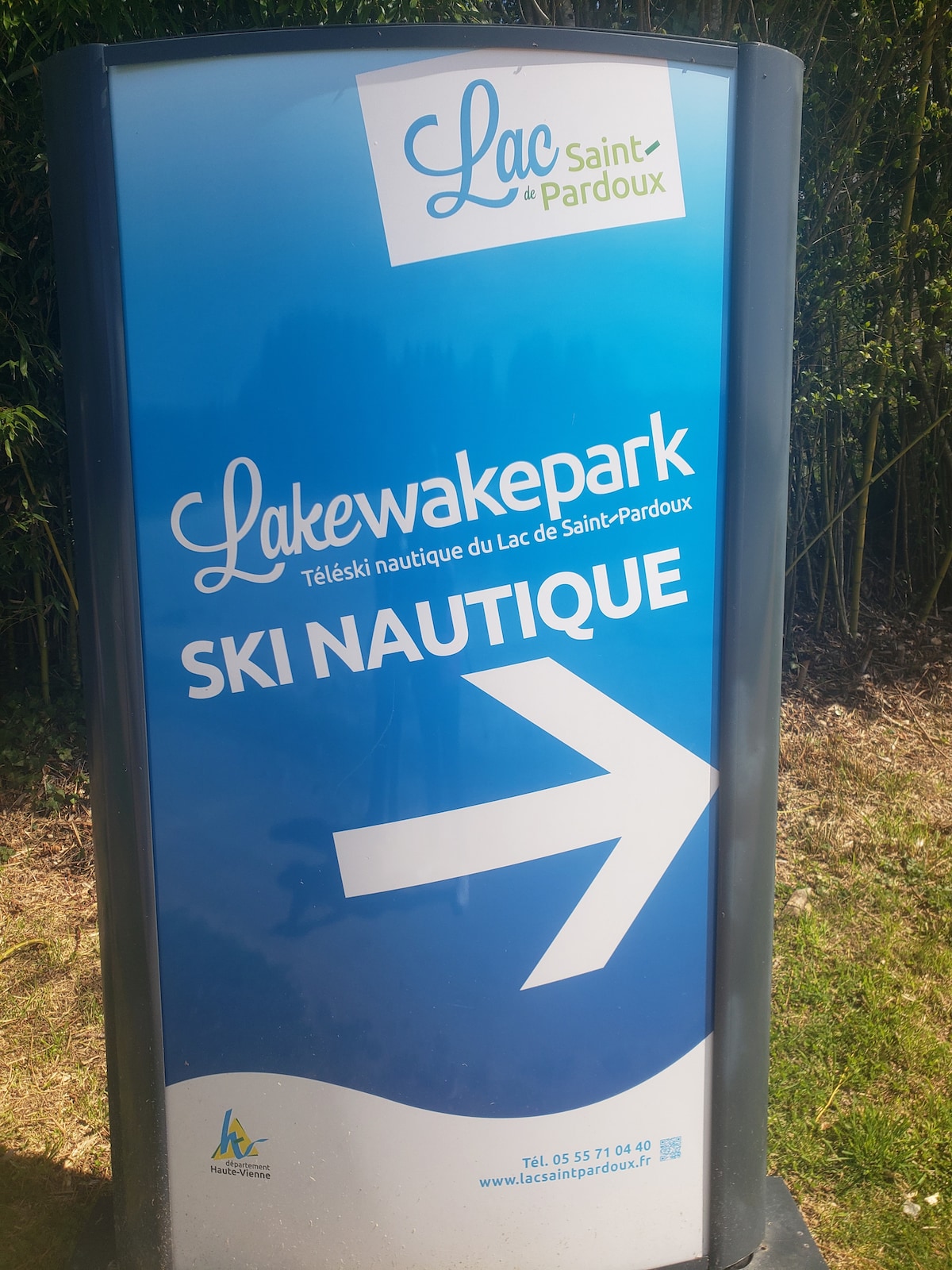 A colorful sign directs visitors to Lake Saint-Pardoux's wake park, featuring an arrow pointing right. The bright blue background prominently displays the name 'Lakewakepark,' with the phrase 'Ski Nautique' highlighted for outdoor enthusiasts.