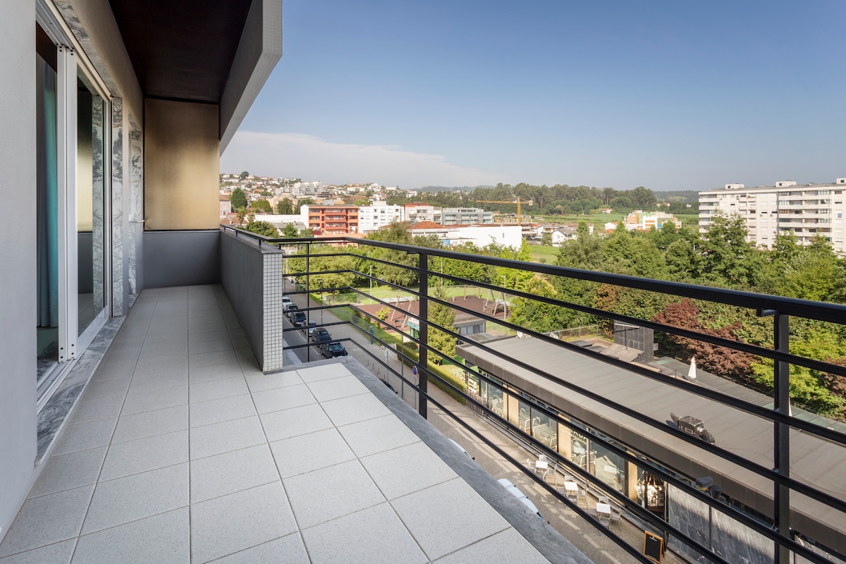 A spacious balcony offers a clear view of the surrounding landscape, featuring well-maintained green areas and buildings in the distance. The tiled floor enhances the outdoor space, with modern railings providing safety and an unobstructed perspective of the scenery.