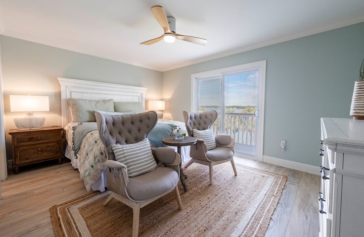 Elegant bedroom with a king-sized bed, warm natural light, cozy seating, and a balcony ideal for peaceful starts and sunset unwinding.