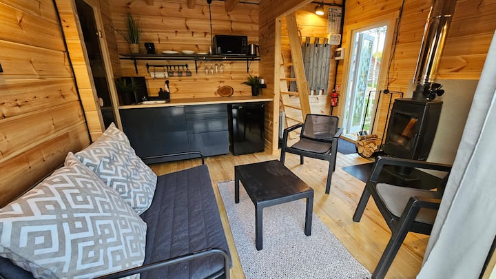 El primer piso de un sauna lounge forestal. Tiene una cocina, sauna, parte de la sala de estar y también una estufa de leña. Aquí puedes encontrar lugares para dormir en el sofá cama plegable con capacidad para 2 personas.