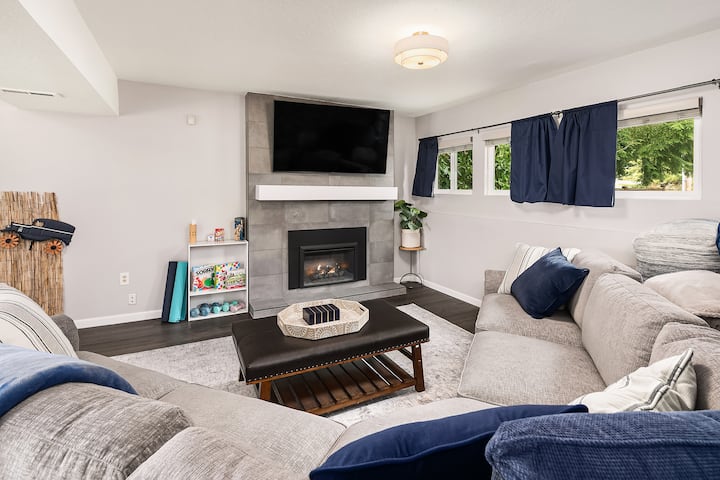 Другата половина от всекидневната на долния етаж с голям, удобен диван с места за сядане на стадиона, телевизор, постелки за йога. Чудесно място да се помотаете с групата си и да гледате филм!