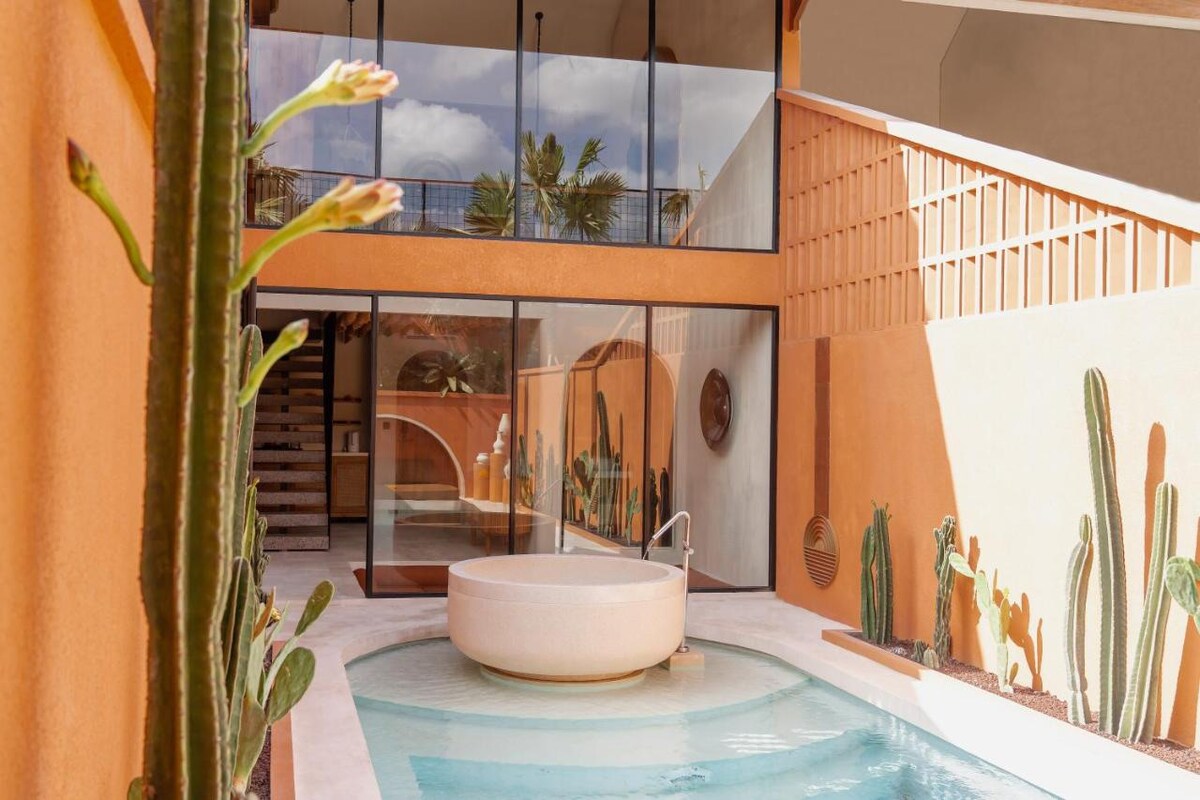 An inviting private pool is framed by smooth walls in warm earth tones. Tall cacti create a natural border, and glass panels reflect the serene atmosphere, allowing for ample sunlight. The space fosters a connection with the outdoors while providing a tranquil retreat.