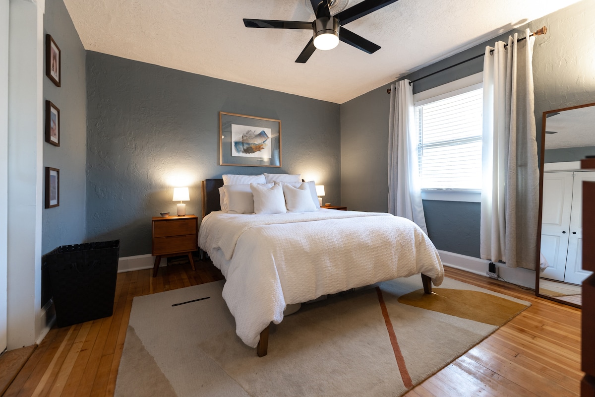 Chumba kikuu cha kulala chenye kitanda aina ya queen na mashuka ya kifahari. Inajumuisha rafu ya mizigo, kizuizi, kabati la kujipambia la droo 4 (linaloonekana upande wa kulia wa sehemu kubwa ya picha), rafu ya nguo na kabati kamili kwa ajili ya kusafiri kwa urahisi.