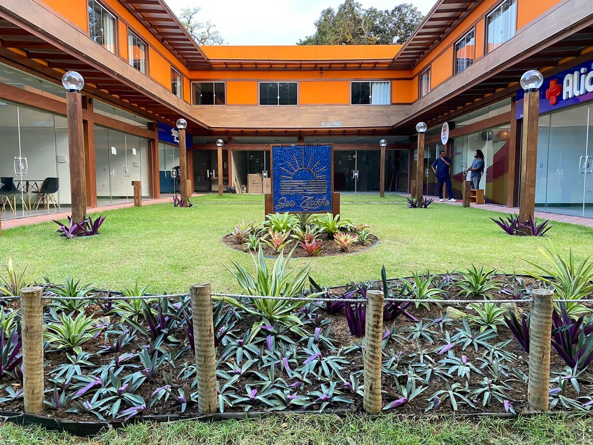 A well-maintained outdoor area features a grassy courtyard surrounded by vibrant plantings, including ornamental foliage. Decorative light globes stand on wooden posts, enhancing the inviting layout. The building's exterior is painted in bright orange, with glass doors leading to various rooms.