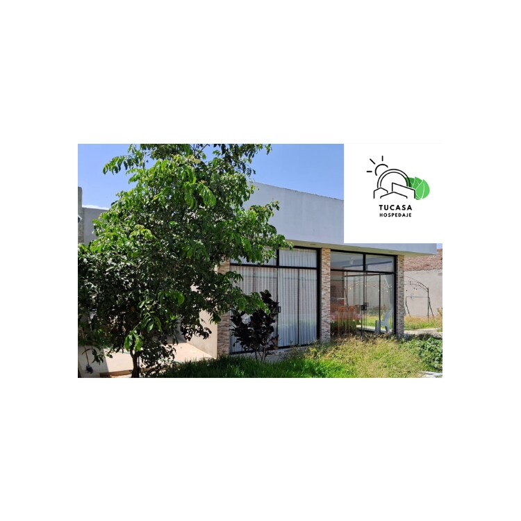 The exterior features a modern design with large glass windows, allowing natural light to fill the space. A well-maintained garden with green foliage surrounds the entrance, contributing to a serene atmosphere. The structure is set against a clear blue sky.