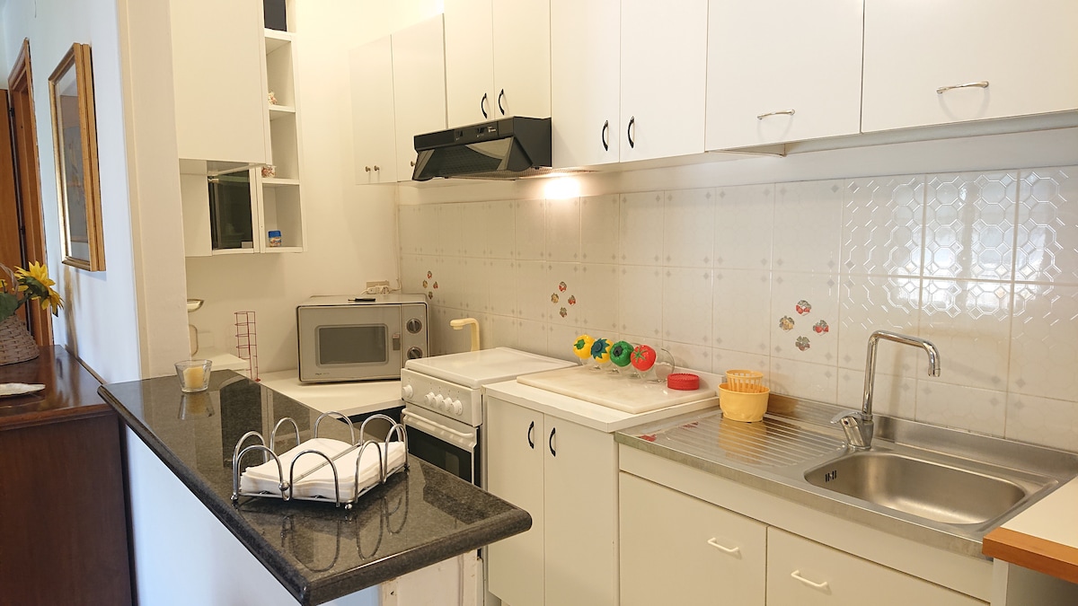 A functional kitchen features white cabinetry and modern appliances, including a microwave and stove. A granite counter provides space for meal preparation, while a sink is situated next to a drainer. Decorative elements, such as colorful accents, add a friendly touch to the area.