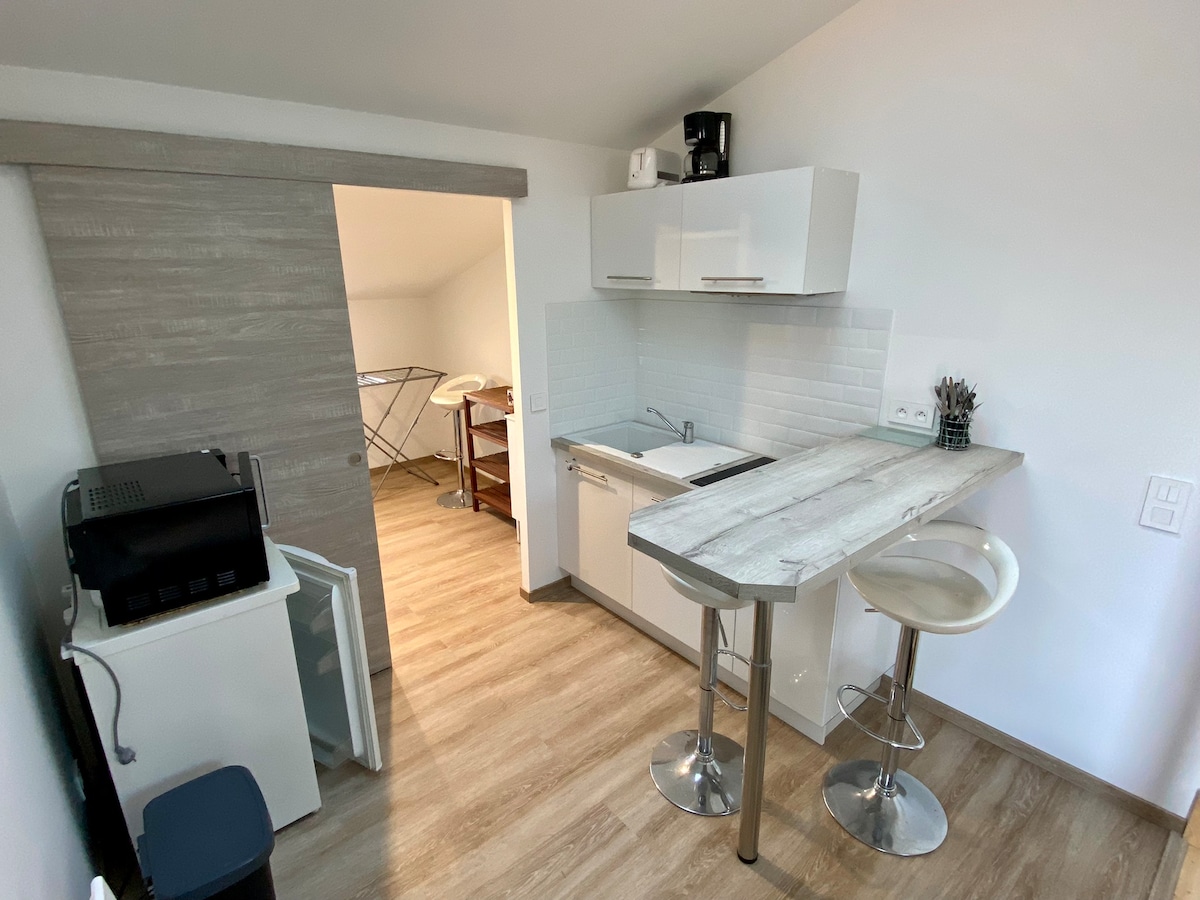 A modern kitchen area is visible, featuring white cabinets and sleek countertops. A two-stool bar allows for casual dining. Adjacent, an informal laundry area with a drying rack is present, providing convenient storage solutions. A coffee maker rests on the countertop.