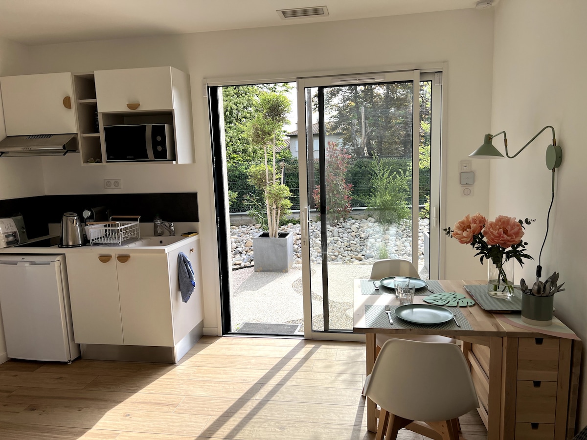 A kitchenette is visible on the left, equipped with essential appliances including a microwave and refrigerator. A small dining table is seen beside sliding glass doors that open to a garden view, with floral arrangements adding a touch of color.
