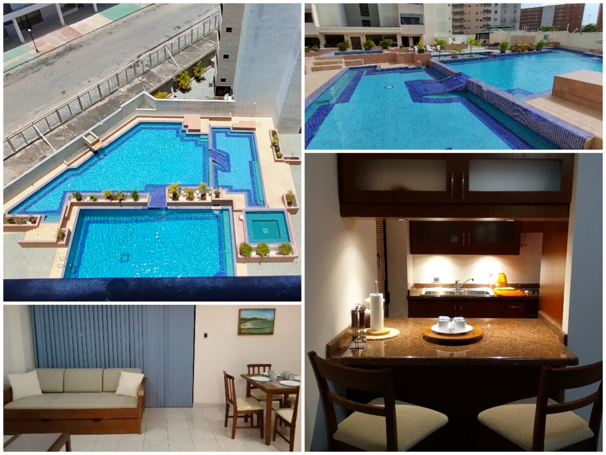 The image displays a spacious pool area, featuring multiple interconnected pools surrounded by terraces. A view of the apartment's kitchen area is included, showcasing wooden cabinets and a countertop with utensils. A living space is presented with a couch and dining table, complemented by light-colored tiles.