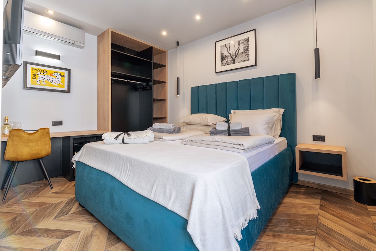 A spacious bedroom is illuminated with soft lighting and features a large king size bed dressed in neutral bedding. A stylish desk is positioned beside the bed, complemented by modern wall art and a sleek storage unit. A cozy atmosphere is created with warm wood flooring.