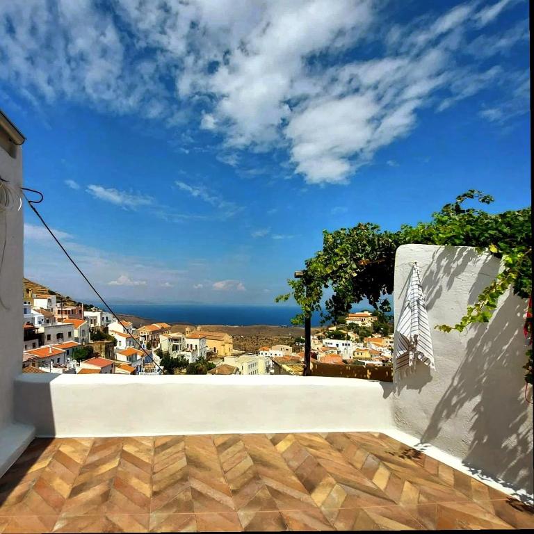 A sunlit terrace features a scenic view of the surrounding town and the sea. The space is adorned with a white towel hanging on a railing, while lush greenery climbs along the wall. A patterned tiled floor enhances the outdoor area.