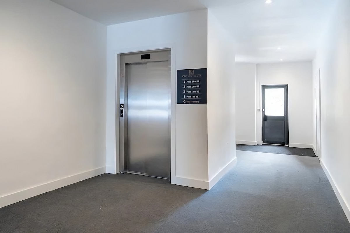 A well-lit corridor is depicted, featuring a sleek elevator on the left side. A directory sign is mounted on the wall, providing helpful information about the building's layout. A door is visible at the far end, leading to another space.