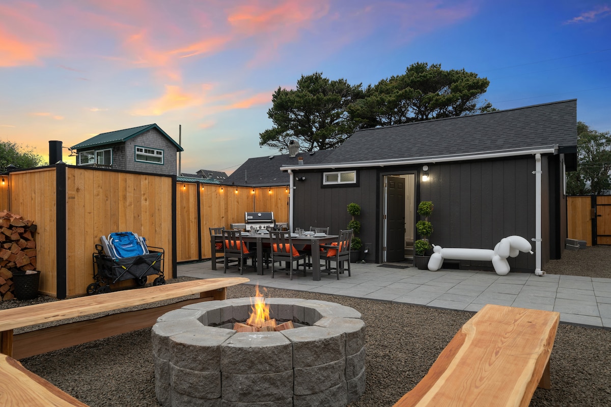 A cozy outdoor space is featured, showcasing a fire pit surrounded by stone seating. Nearby, a dining table with multiple chairs is set up for al fresco meals. The backyard is enclosed by wooden fencing, creating a private atmosphere, with warm lighting enhancing the serene setting.