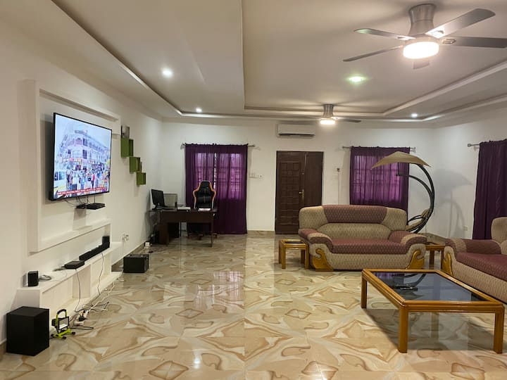 Picha iliyo hapo juu inaonyesha sebule ya fleti kuu iliyo na makochi na televisheni ya inchi 75 iliyo na baa za sauti na kituo cha kazi.