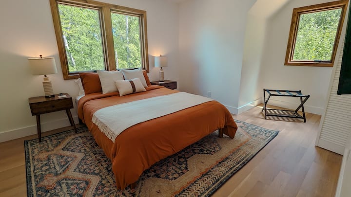 غرفة نوم في الطابق العلوي بسرير بحجم كوين ومصابيح منفذ شحن USB وتلفزيون بشاشة مسطحة.