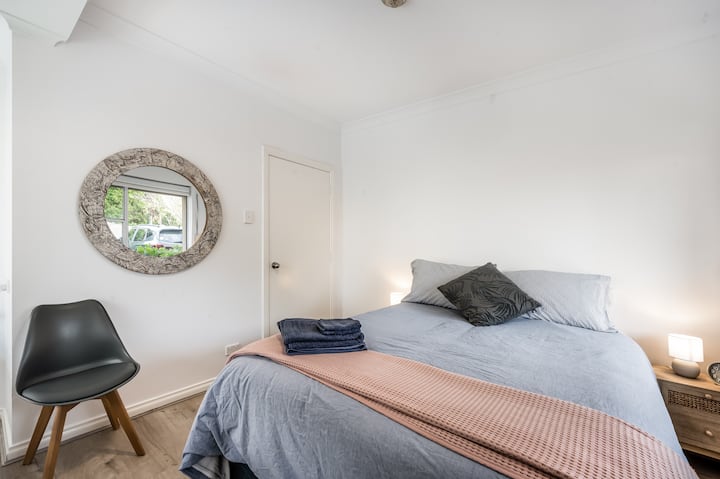 Bračni krevet sa svježom posteljinom u nježnim tonovima stvara ugođaj mira, a prostoriju krase tamne zavjese i ugrađeni ormari, a kroz prozore prodire jutarnje svjetlo.