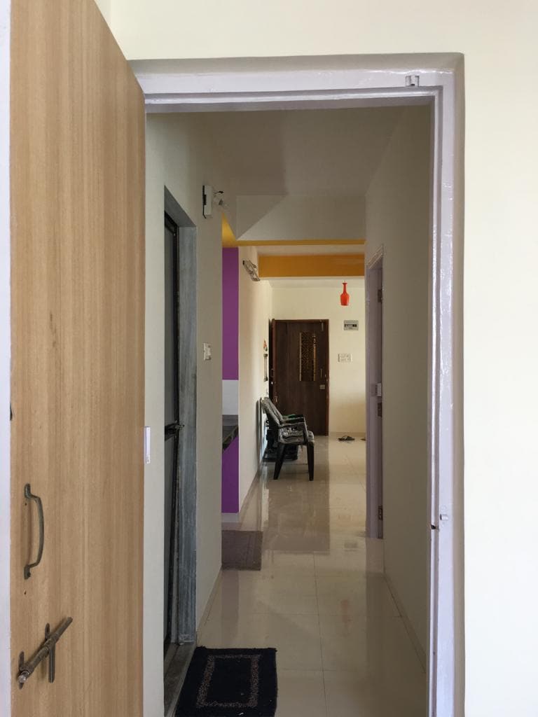 An open doorway reveals a hallway leading to several rooms. Light-colored walls provide a bright atmosphere, and a dark chair is visible to the left. The space features smooth flooring and a welcoming entrance, enhancing the appeal of the apartment.