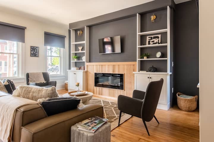 Მისაღები ოთახი ტყავის დივნით, მრგვალი ყავის მაგიდით, შავი სავარძლით, კედელზე მიმაგრებული ტელევიზორითა და თანამედროვე ბუხრით