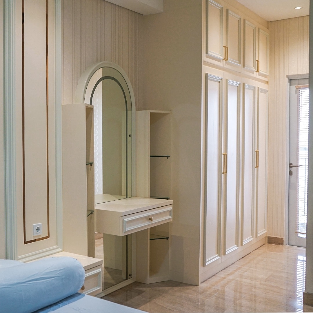 A well-appointed area features a mirrored vanity with a drawer and shelving, complemented by built-in cabinets with gold handles. The light-colored walls and marble flooring contribute to a bright and open ambiance.