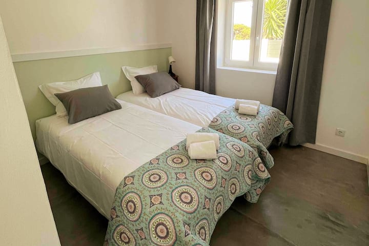 Dormitorio con dos camas individuales, ambiente luminoso y decoración suave, ropa de cama y toallas cómodas incluidas, ideal para descansar en una casa de playa.