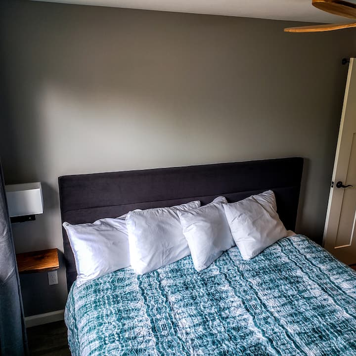 Bedroom three features  1 king bed, 1 floating nightstand, 1 wall mounted reading light with integrated plugin, bathroom in the hall, a 50" smart TV and ductless heat/cool system.