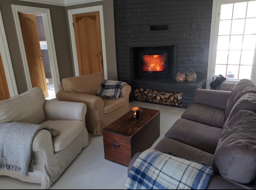 A spacious living area is featured, showcasing a cozy seating arrangement with multiple armchairs and sofas. A wooden coffee table sits in the center, while a fireplace is prominently positioned against a dark feature wall, creating a warm focal point for the room.