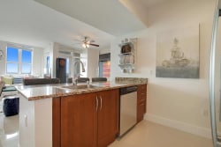 The modern kitchen features a spacious granite countertop with a built-in sink and stainless steel appliances, including a dishwasher. A large window allows natural light to fill the space, while decorative wall art enhances the atmosphere.