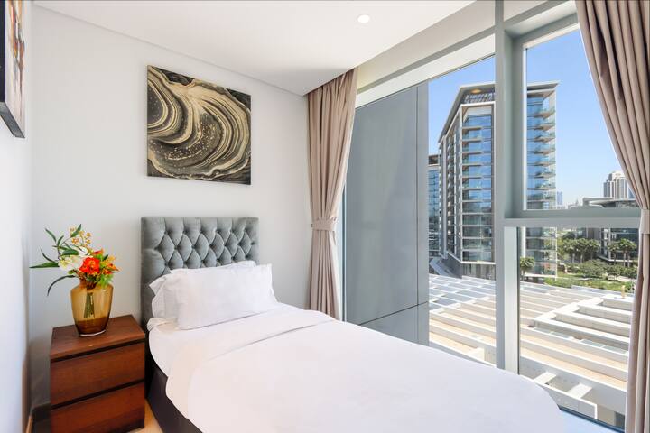 ห้องนอนเดี่ยวสว่างสดใส มีหัวเตียงหรูหราและหน้าต่างสูงจากพื้นถึงเพดานที่มองเห็นวิวเมือง