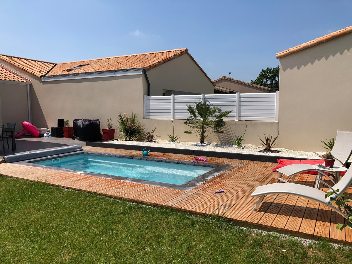 A private pool area is showcased, featuring a rectangular pool bordered by wooden decking. Sun loungers are positioned nearby on a grassy lawn, with potted plants and small shrubs adding greenery. The surrounding fencing ensures privacy, creating a serene outdoor environment.