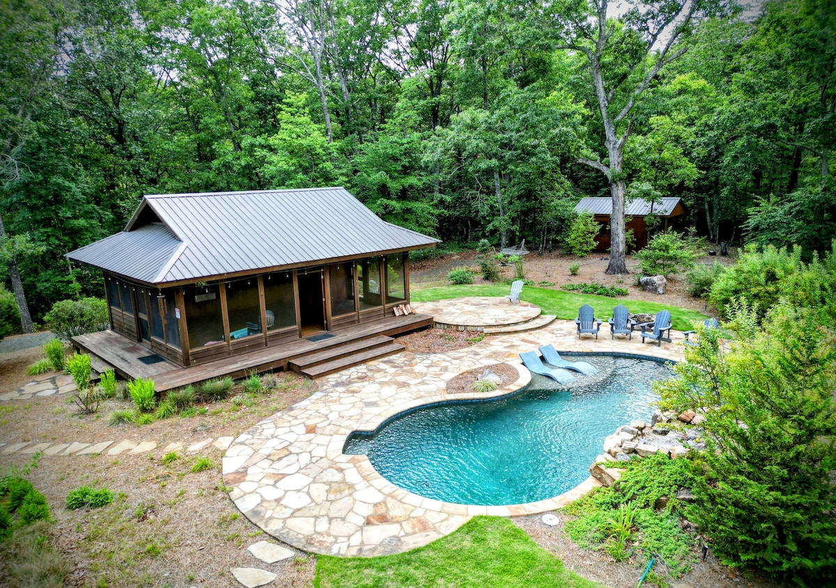 An aerial view showcases the outdoor casita beside a uniquely shaped saltwater pool. Surrounding greenery provides a natural backdrop, while a stone patio accommodates lounge chairs arranged for relaxation. The gentle curves of the pool and stone pathways enhance the serene outdoor environment.