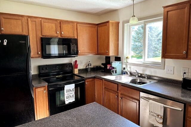 A well-equipped kitchen features wooden cabinetry and dark countertops. Appliances include a black microwave and an oven, arranged alongside a modern sink beneath a window that allows natural light to fill the space. Utensils and a coffee maker are conveniently situated on the countertop.