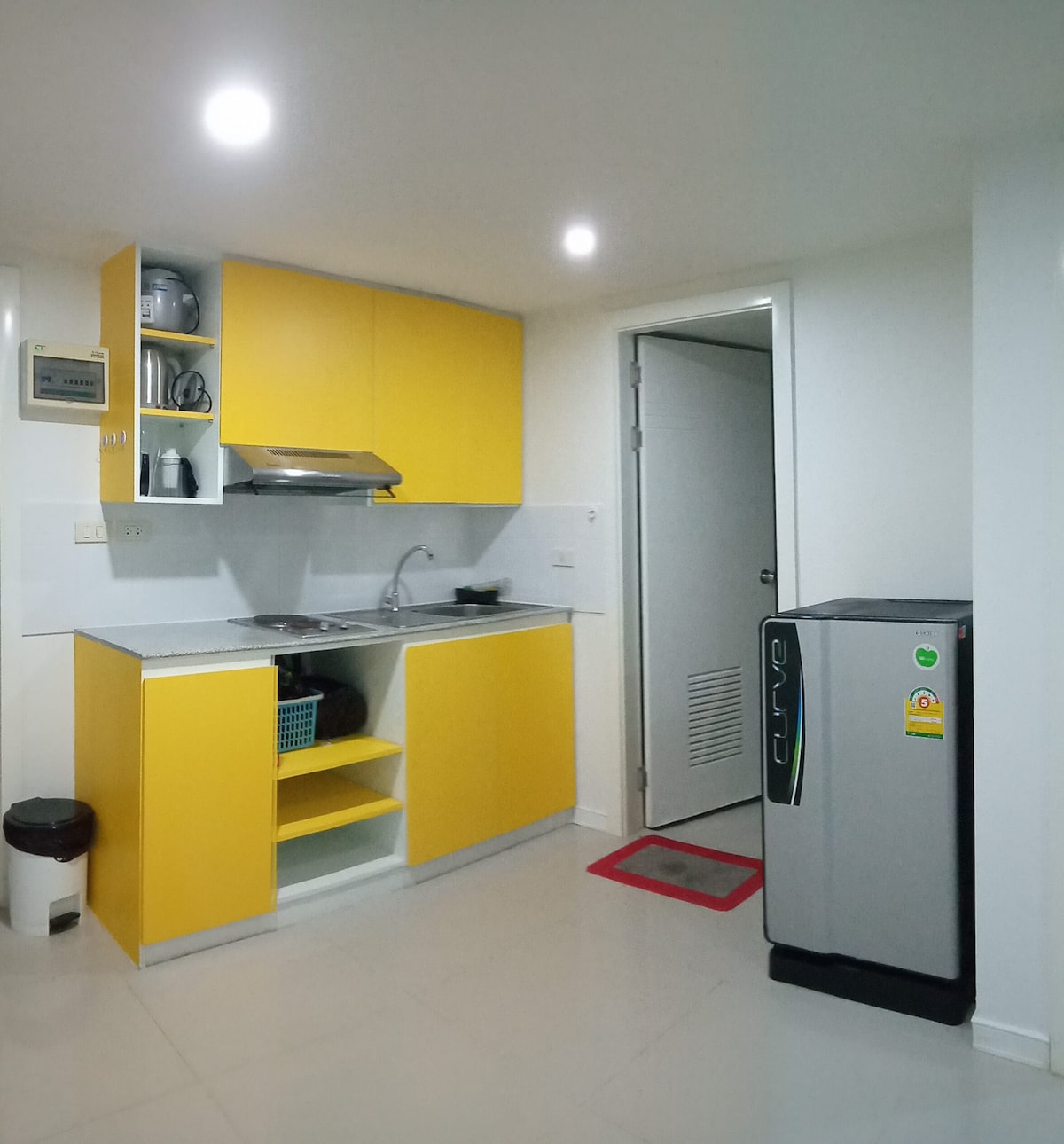 A modern kitchen area is presented with bright yellow cabinetry and a sleek countertop. Essential appliances are included, such as an electric stove and a refrigerator. The space is well-lit with recessed ceiling lights, contributing to a functional and inviting atmosphere.