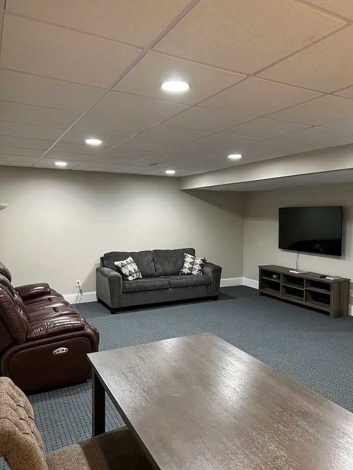 בסלון יש כורסת עור דו - מושבית, ספה נפתחת רחבה וטלוויזיה חכמה 65 אינץ' מבית Samsung.