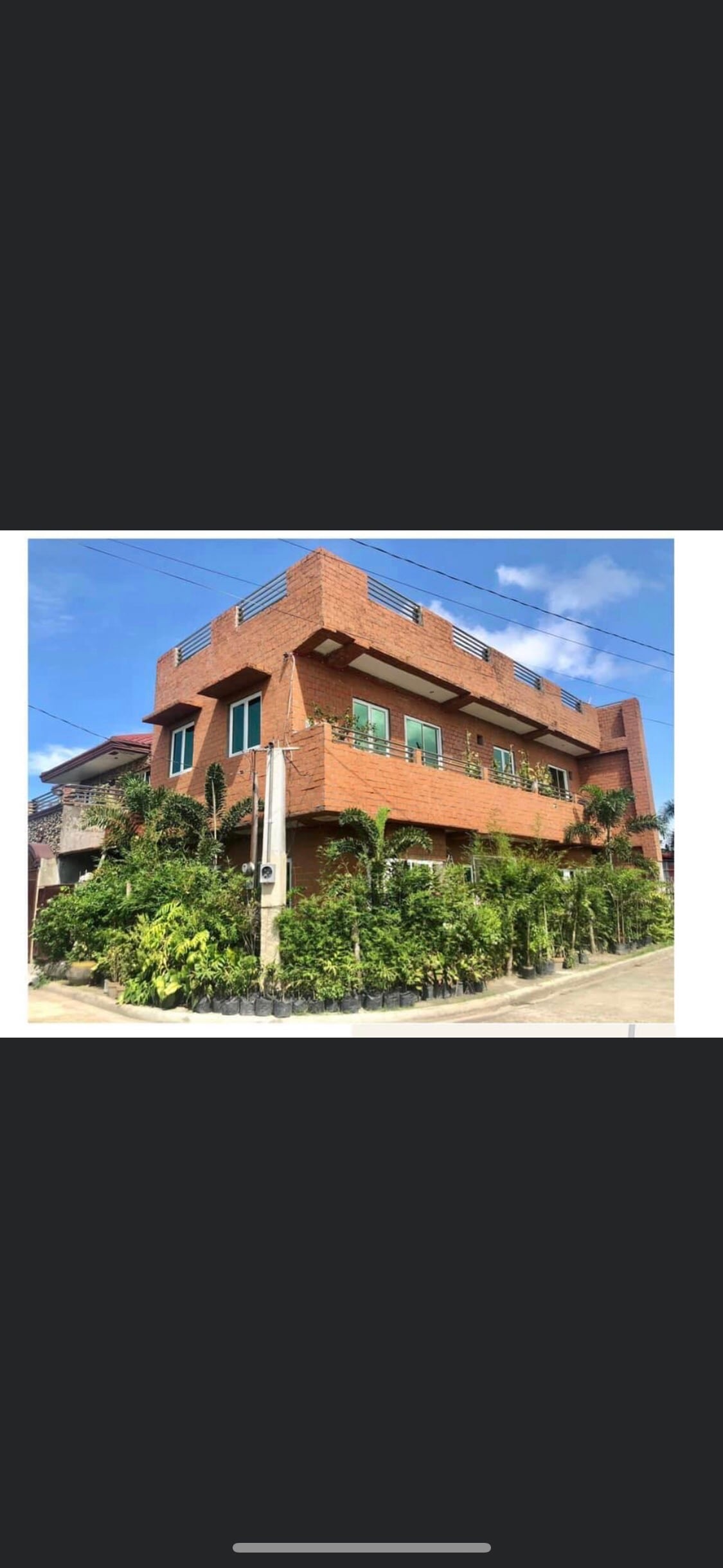 A three-story brick building is surrounded by lush greenery, with colorful window shutters enhancing its charm. The architectural design features a combination of straight lines and angular elements, while clear blue skies provide a bright and welcoming backdrop.